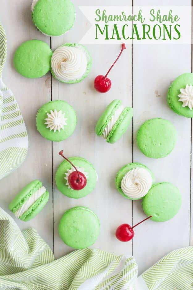 Bright green macarons with white cream filling on white wood with maraschino cherries and a green cloth