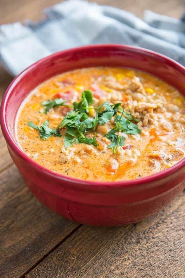 Creamy buffalo chicken chili in a deep red bowl topped with chopped cilantro on a weathered wooden table