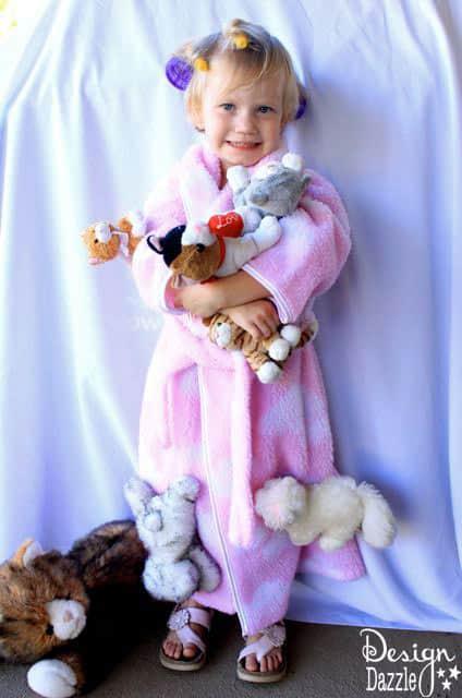 Child wearing a bathrobe covered with plush cats and hair rollers in a DIY Cat Lady costume with source watermark