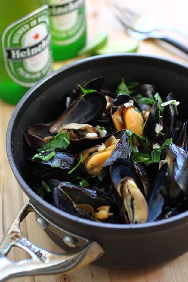 Beer steamed mussels in a black pan with chopped parsley, two green beer bottles standing behind it.