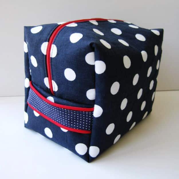 Boxy fat quarter toiletry bag in navy and white polka dots with a red zipper and a red piped band across the side
