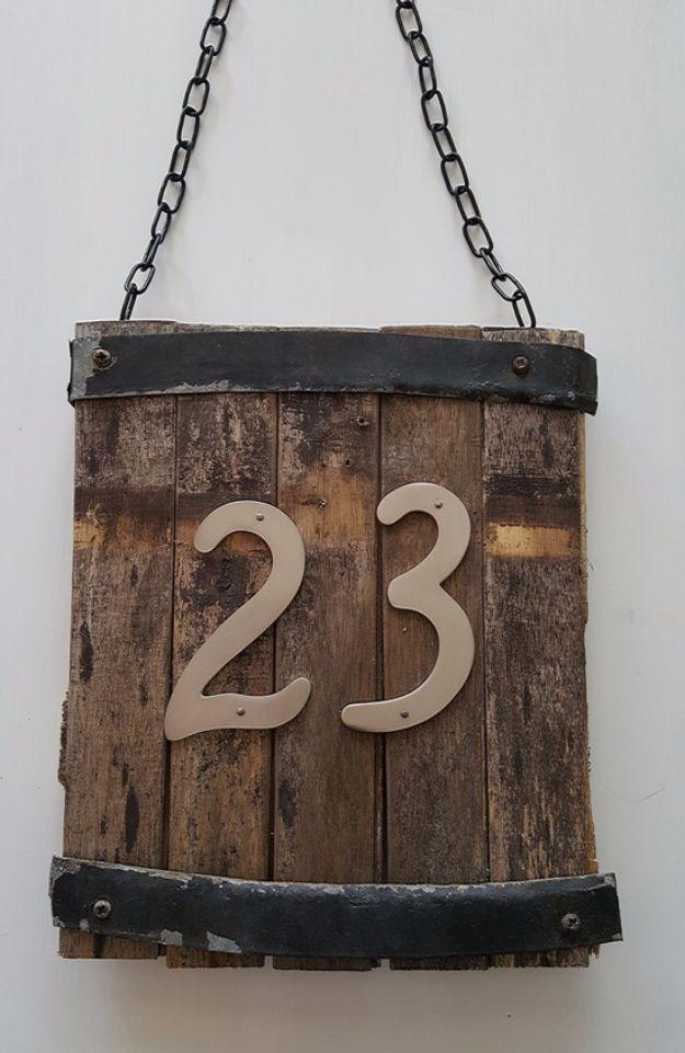 A stained cedar board mounted with dark metal house numbers, hung beside a front door under a porch light