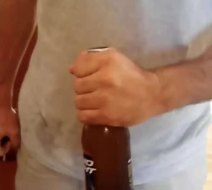 Easy way to open a beer bottle using a car key, hand gripping the bottle high on the neck with the cap flush