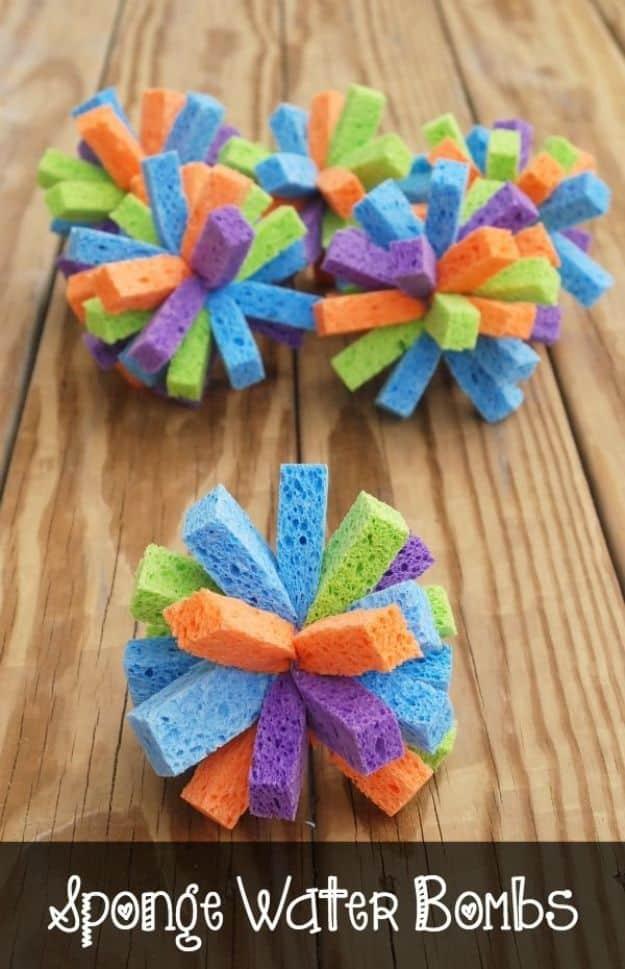 Three sponge water bombs made from bright cut sponge strips tied at the center, lying on wooden decking