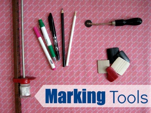 Assorted fabric marking tools including chalk, pencils, markers and a tracing wheel on pink background