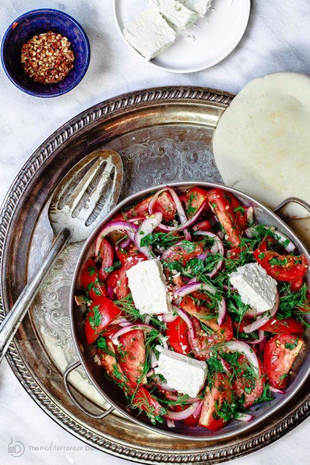 Mediterranean tomato salad, red tomato wedges with herbs and white feta in a bowl on a silver tray with a dish of sumac