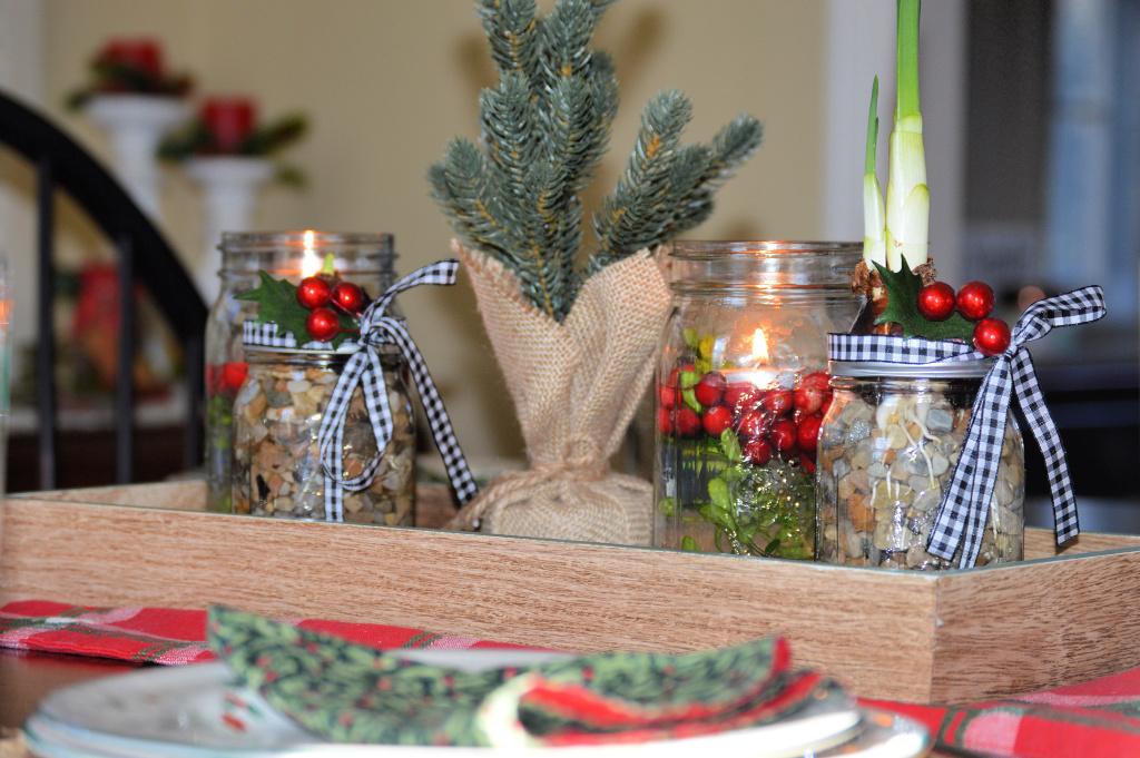 A wood tray holding mason jars with river rocks and paperwhite bulbs, a cranberry candle jar and a burlap wrapped mini tree