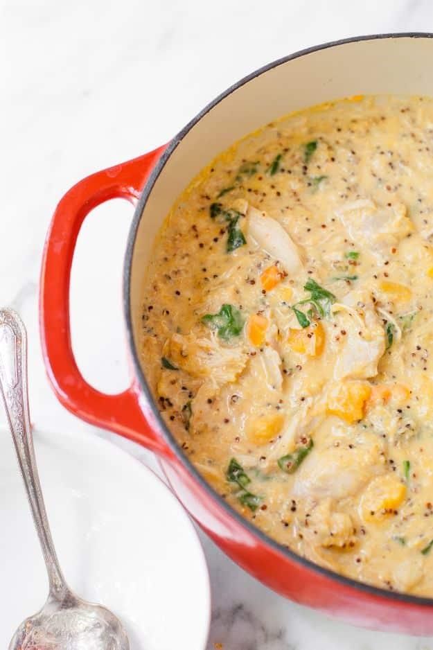 Red enameled pot of creamy chicken pumpkin chowder with quinoa and spinach, a silver spoon beside it