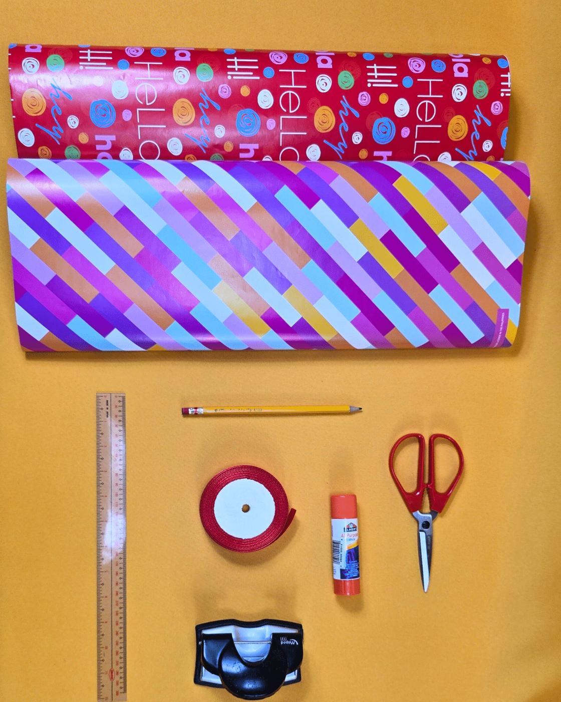 DIY Paper Crafts - wrapping paper rolls, ruler, pencil, ribbon, glue stick, scissors and hole punch laid out on yellow