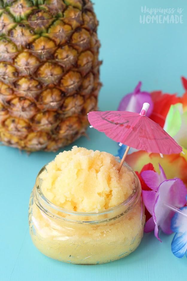 Pina colada sugar scrub, a yellow scrub in a jar with a whole pineapple, a paper umbrella and flowers