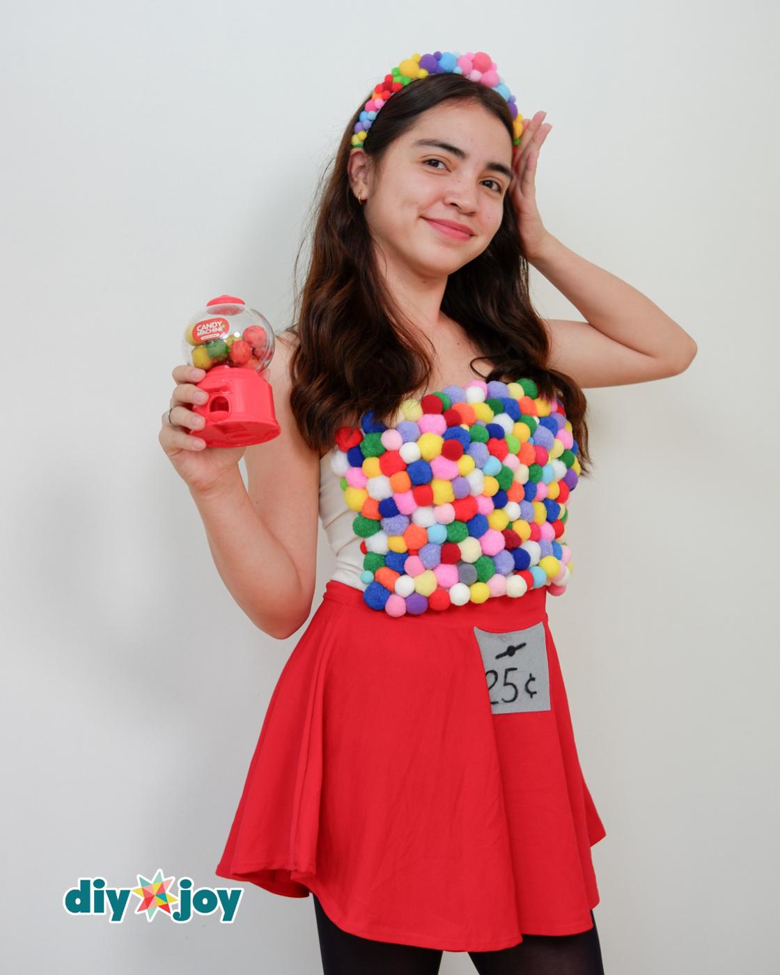 DIY Crafts - model in an easy Halloween costume, raising the toy gumball machine while wearing the pom pom top and skirt.