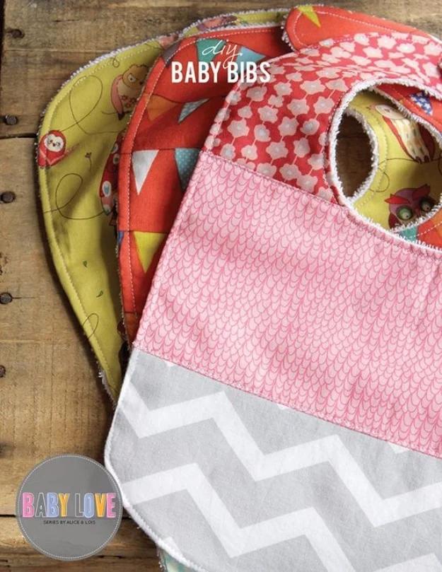 Four baby bibs in owl, bunting and floral cotton prints with terry backing, stacked on weathered wood