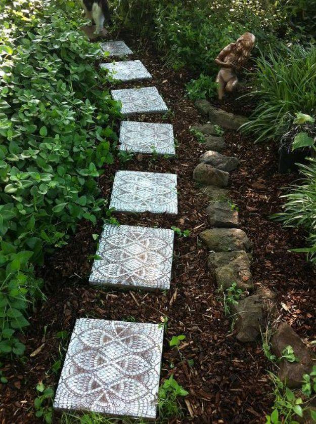 Square concrete stepping stones sprayed with a white lace doily pattern running through a shady garden