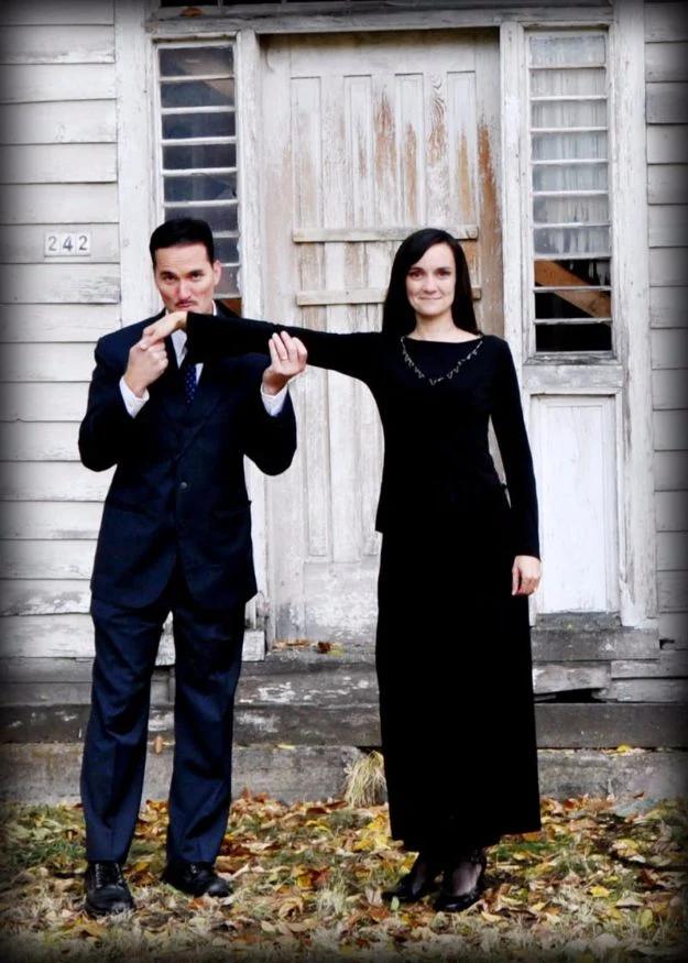 Gomez and Morticia Addams couples costume with a dark suit and thin mustache beside a long black gown