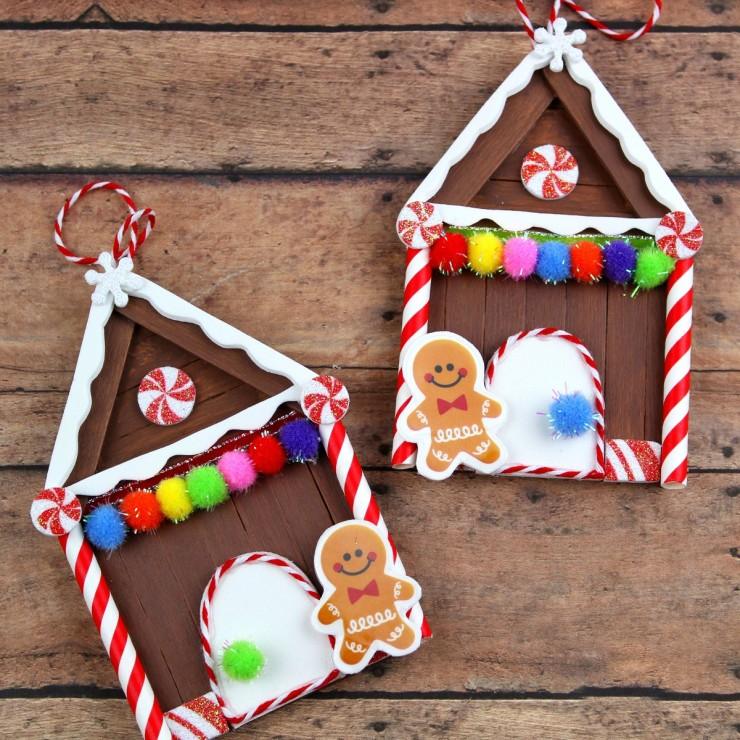 Two popsicle stick gingerbread house ornaments with white foam icing, pom pom gumdrops and paper straw candy canes