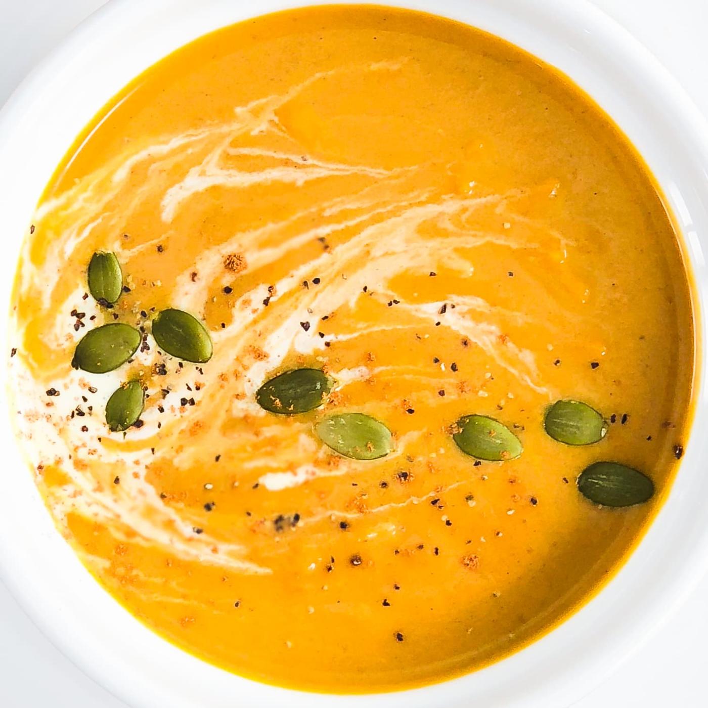Instant Pot pumpkin soup in a wide bowl, bright orange with a cream swirl, pumpkin seeds and cracked pepper