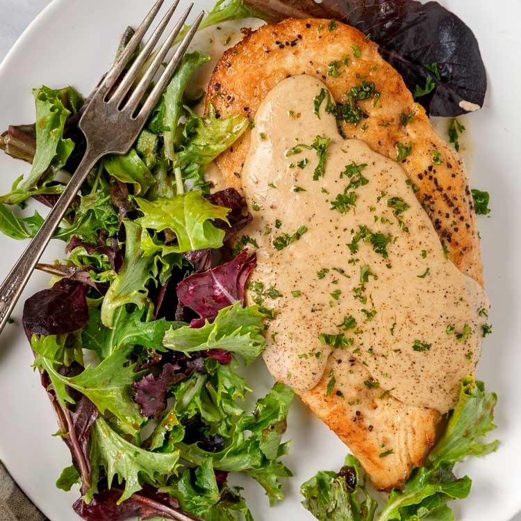 Creamy roasted garlic chicken, a chicken breast under pale cream sauce with parsley, served over mixed greens