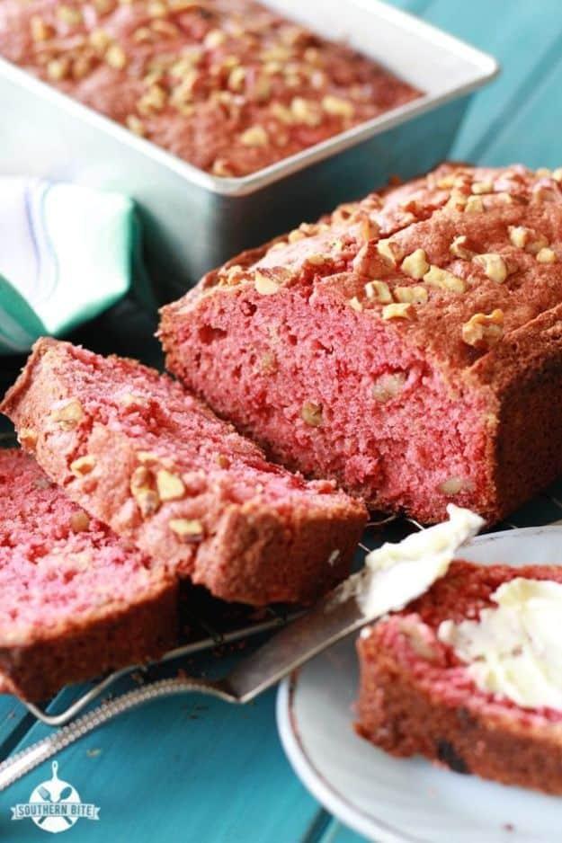 Sliced strawberry bread with pecans on a cooling rack, pink crumb visible, butter spread on the cut slice