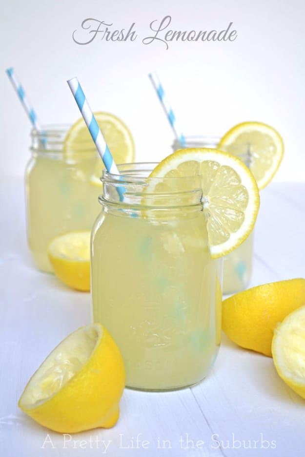 Three mason jars of pale fresh lemonade with blue striped straws and lemon wedges on a white surface