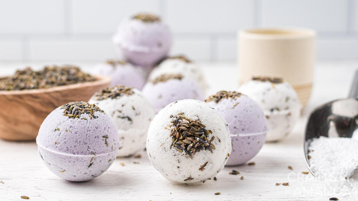 Purple and white lavender bath bombs topped with dried lavender buds in a wood dish and on a white counter