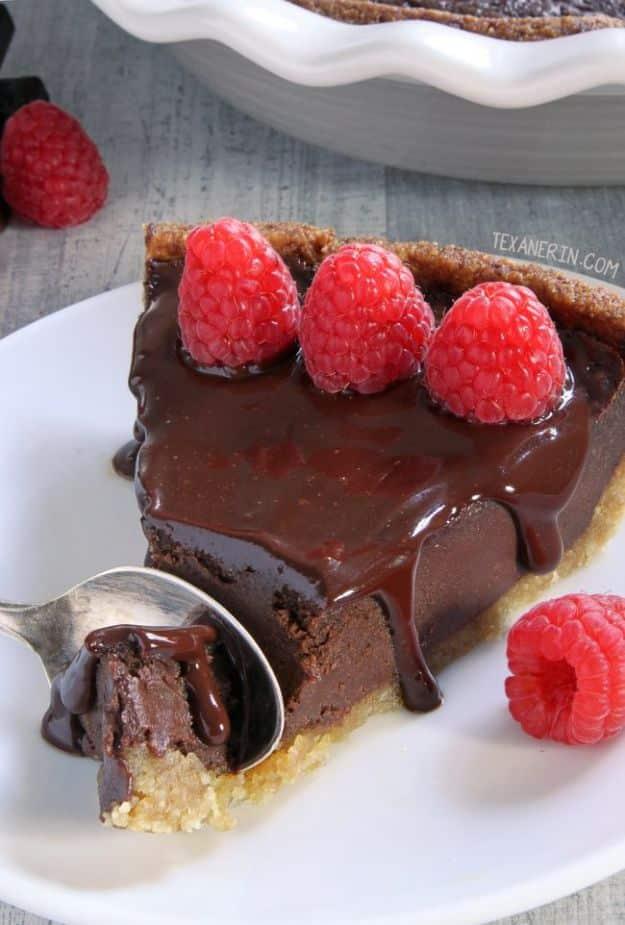 Paleo chocolate fudge pie slice topped with fresh raspberries, a spoon lifting a bite of the dense filling