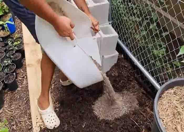 Gravel poured and leveled into the dug out hole that forms the compacted base for a DIY cinder block plant shelf