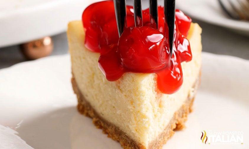 Plain cheesecake slice topped with glossy cherry sauce on a white plate in a finished dessert close-up
