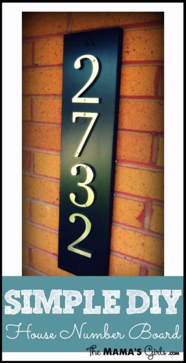 Simple DIY house number board in black with silver vertical numbers, mounted on an orange brick wall