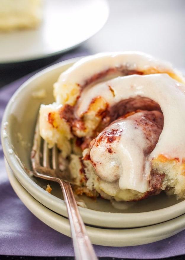 Cinnabon copycat cinnamon rolls in a baking dish under thick white cream cheese frosting, pulled apart