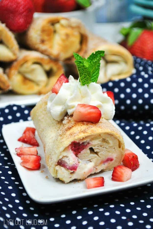 Strawberry cheesecake chimichanga cut open on a white plate with whipped cream, mint and chopped berries