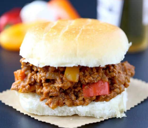 Sloppy joe on a soft white bun with peppers and tomato visible in the meat, dark background behind it