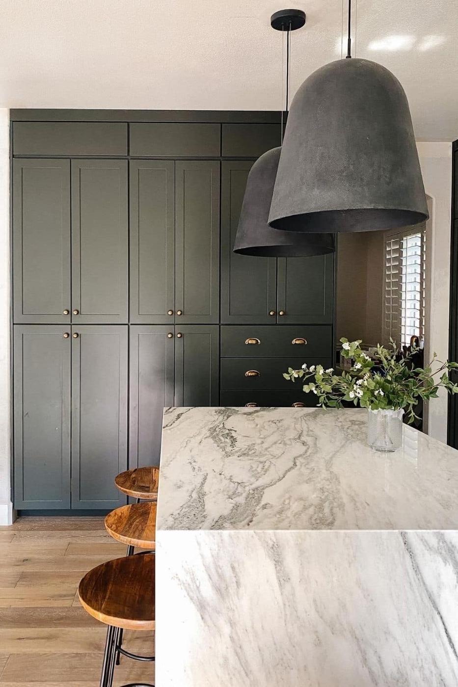 Deep green kitchen cabinets running to the ceiling with two dark dome pendant lights over a white marble island
