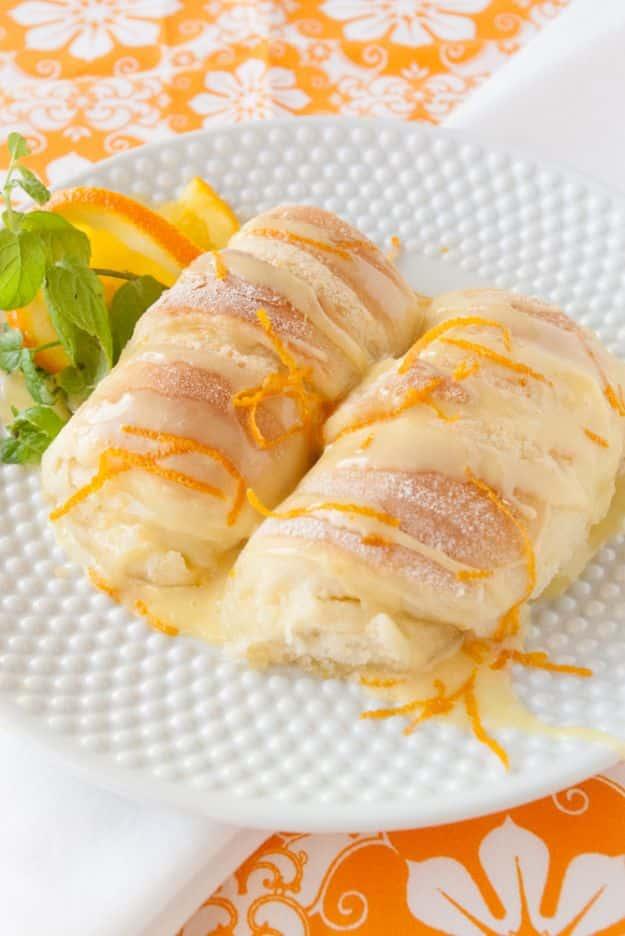 Orange sweet rolls glazed and topped with fresh orange zest on a white plate with orange fabric behind