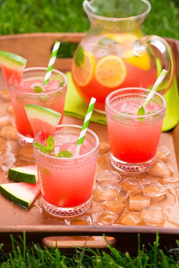 A tray of watermelon lemonade glasses with watermelon wedges, mint and striped straws set out on grass