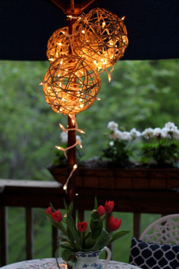 Glowing twine ball lanterns strung with fairy lights hanging above a deck railing planted with red tulips