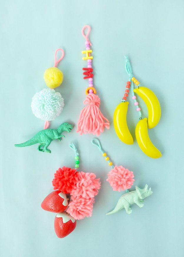 Painted plastic dinosaur, banana and strawberry luggage tags strung with yarn, pom poms, tassels and letter beads