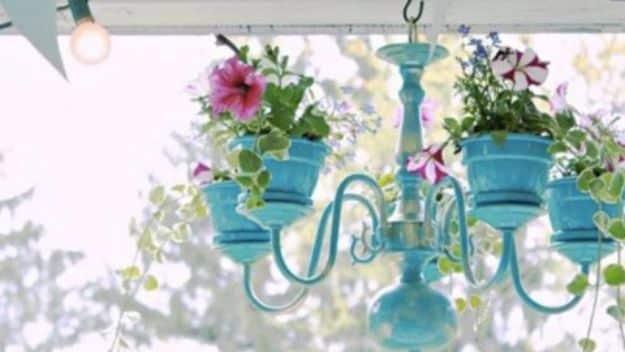 Old chandelier turned outdoor planter painted turquoise with small pots of pink and white flowers on a porch