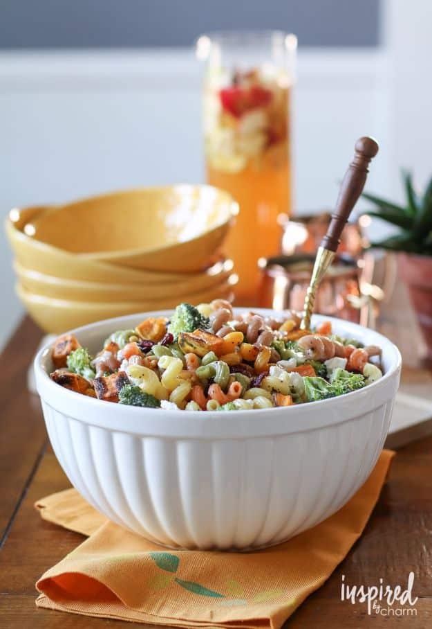 Fall harvest pasta salad in a white bowl with multi colored pasta, broccoli, cranberries and a wooden spoon