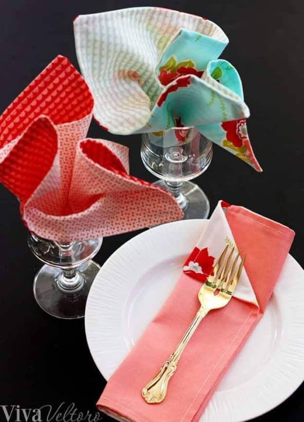 Five minute cloth napkins in red waffle, coral and aqua floral prints, three standing in wine glasses beside a gold fork