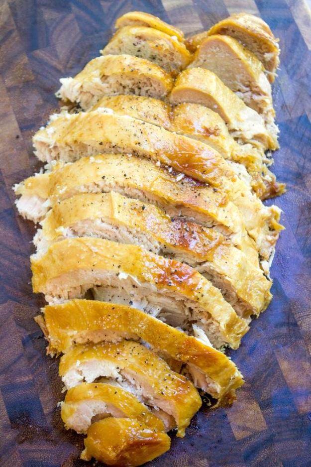 Sliced cooked turkey breast with golden skin arranged on a wooden serving board for a Thanksgiving centerpiece