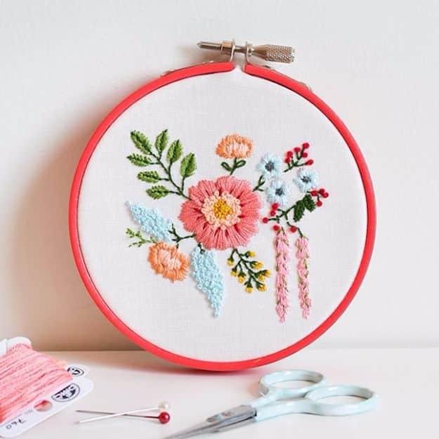 Coral embroidery hoop holding a stitched bouquet of pink, blue and apricot flowers with green leaves, scissors below