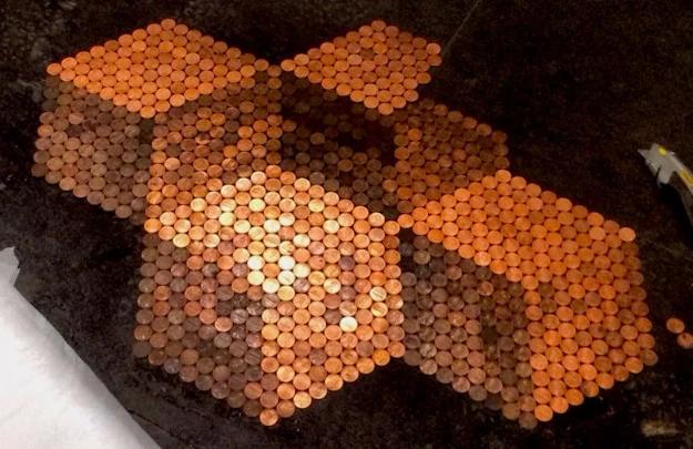 Penny tile floor part laid in hexagonal copper blocks across bare subfloor, with gaps still open in the pattern