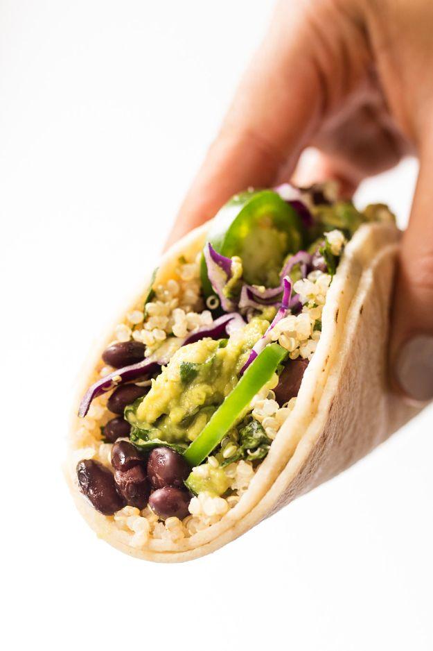 A hand holding a soft corn tortilla taco filled with lime quinoa, black beans, guacamole and red cabbage