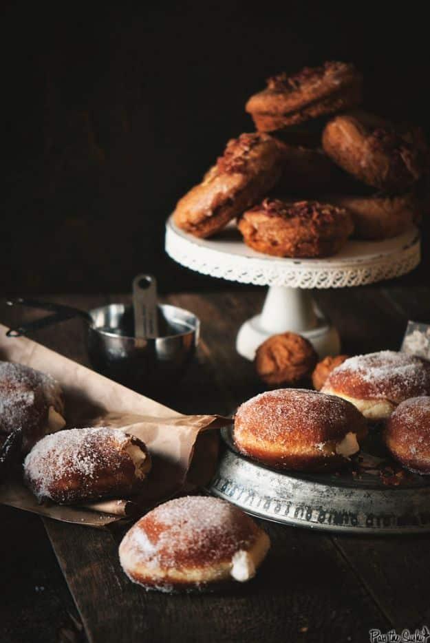 Sugar dusted Irish cream doughnuts split to show the filling, with more on a white pedestal cake stand