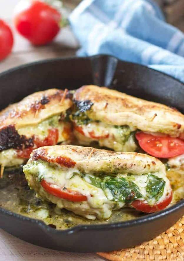 Pesto mozzarella and tomato stuffed chicken breasts in a cast iron skillet, tomato and spinach in the pesto filling