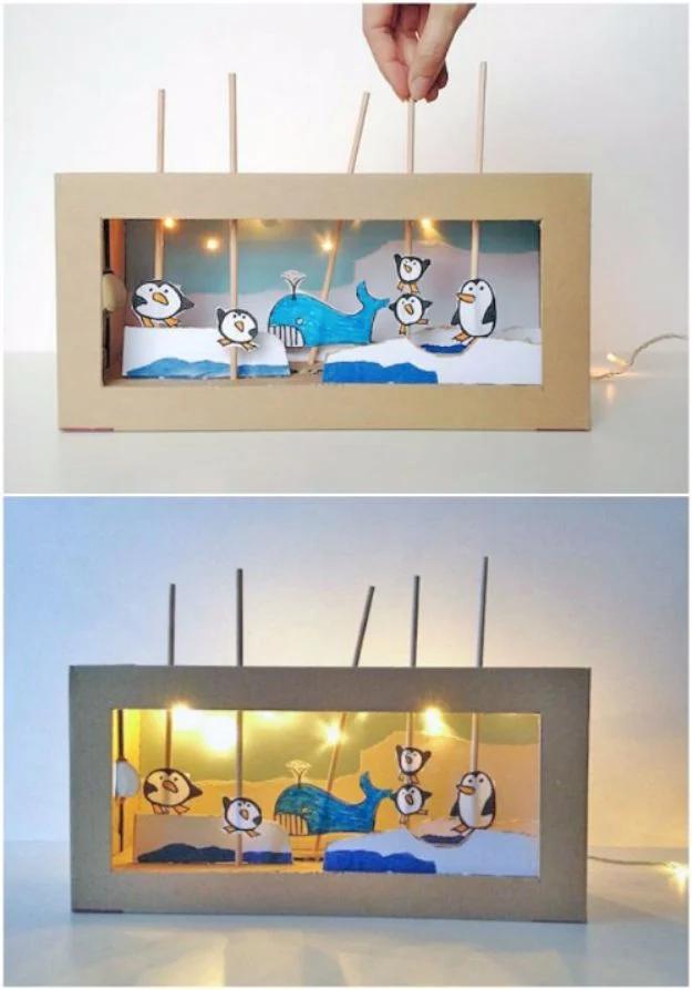 Shoe box puppet theater with a cut out stage, paper arctic scenery and small puppets on skewers, lit inside