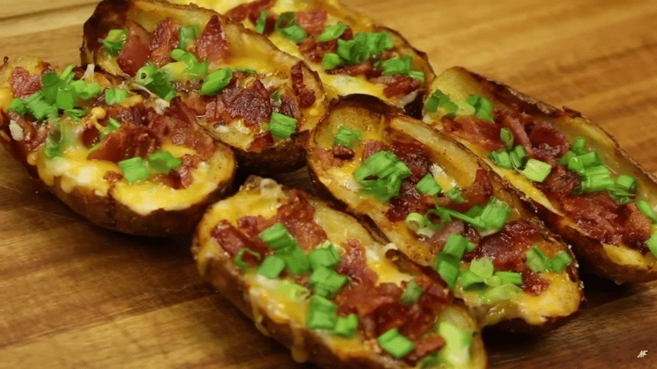 Baked potato skins filled with melted cheese, crisp bacon and chopped green onion on a wooden serving board