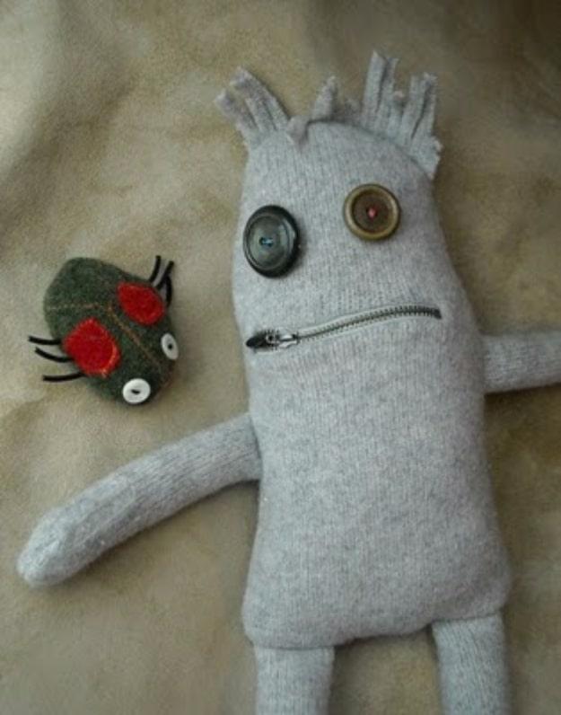 Gray felted wool monster plush with two mismatched button eyes and a zipper mouth lying beside a small green felt bug