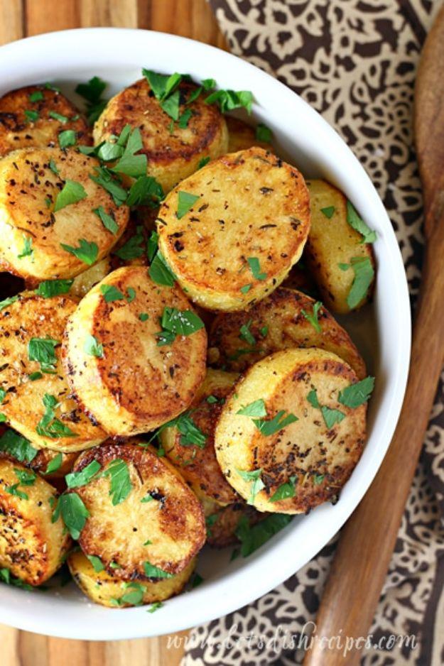 White bowl of thick browned roasted potato rounds scattered with chopped parsley on a patterned cloth