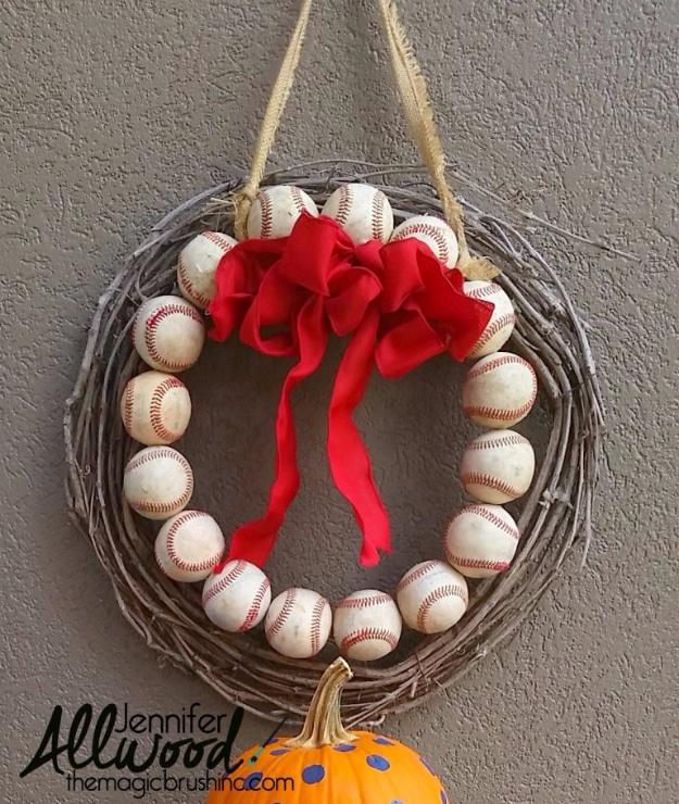 Grapevine wreath ringed with real baseballs and a wide red ribbon bow, hanging on a stucco wall above a pumpkin